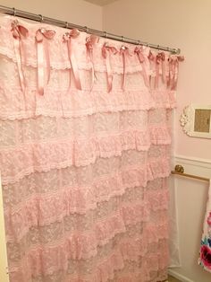 a pink shower curtain with ruffles and bows hanging from it's side