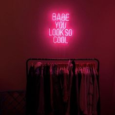 a neon sign that says babe you looks so cool on the wall above a rack of clothes