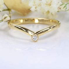 a yellow gold ring with a diamond on it and white flowers in the back ground