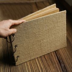 a person holding an open book on top of a wooden table