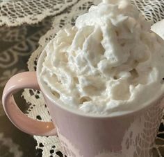 a pink cup filled with whipped cream sitting on top of a doily covered table