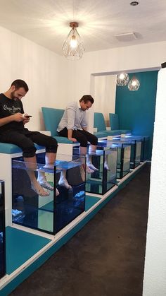 two men sitting on top of blue and white aquariums looking at their cell phones