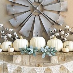 white pumpkins and cotton flowers are arranged on a mantle in front of a windmill