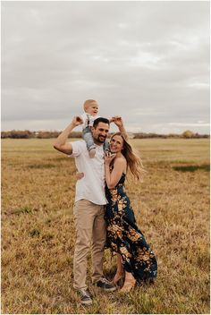 a man and woman holding a baby in their arms while standing in an open field