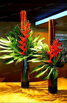 two vases filled with red flowers on top of a wooden table next to bamboo poles