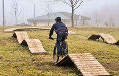 a man riding a bike over some wooden steps in the grass with benches behind him