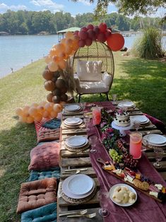 a table set up with balloons and plates for an outdoor party by the water,