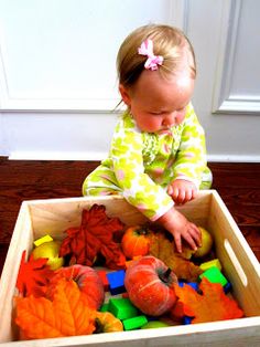 a toddler playing with autumn leaves in a wooden box