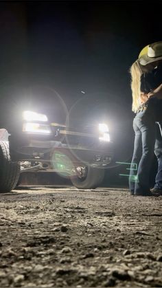 two people standing in front of a truck at night with their headlights on and one person holding the hood up