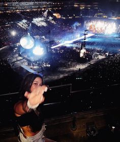 a woman standing in front of a crowd holding her hands out to the side with lights on