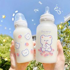 someone holding two baby bottles in front of a blue sky with white clouds and stars