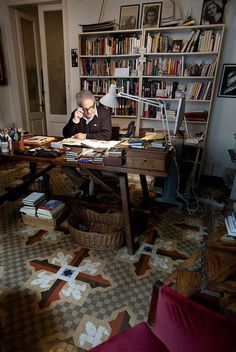 a man sitting at a desk in front of a bookshelf talking on the phone