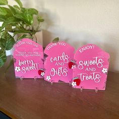 three pink signs sitting on top of a wooden table next to a potted plant