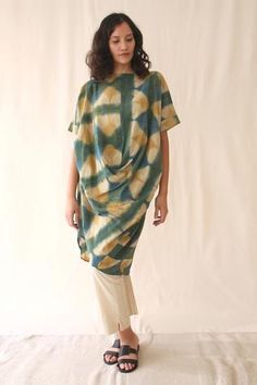 a woman standing in front of a white backdrop wearing a green and yellow tie dye dress