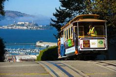 a cable car with people on it going down the road near water and mountains in the background