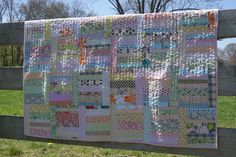 a quilt hanging on a wooden fence in the grass with trees in the back ground