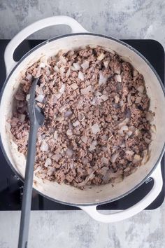 a large pot filled with meat and onions on top of a stove burner next to a spatula