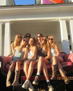 a group of women sitting on top of a red couch in front of a white house