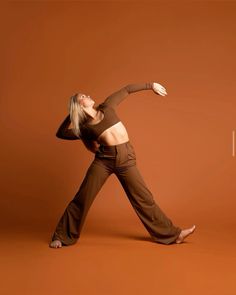 a woman in brown pants is dancing on an orange background