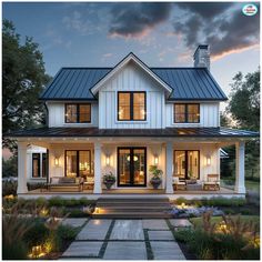 a large white house with lots of windows and lights on the front porch, surrounded by greenery