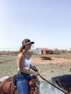 a woman riding on the back of a brown and white horse next to a field