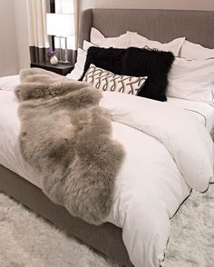 a bed with white and black pillows and blankets on it, next to a window