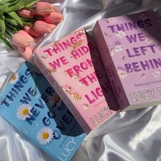 three books sitting on top of a bed next to tulips and pink flowers