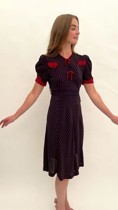 "This is a very special dress, it is so stylish! It is one of my favourite ever 1930s dresses that I have ever had in my collection. It dates from the late 1930s and is made from a navy blue coloured silk crepe with red chevron patterned striped highlights. The design features two faux pockets to the front bodice which are complemented by the red sleeve embellishments and piping to the neckline and pretty puffed sleeves. There are two ties to the front and it retains its original navy and red chevron striped belt at the waist. The dress opens and closes with press studs on one side at the waist and there are three press studs to the bodice so that you can wear the neckline open or closed. This is one of several dresses in my collection that came from a private family collection of antique Vintage Red Midi Dress For Evening, Retro Navy Dress For Formal Occasions, Navy Retro Dress For Formal Occasions, Navy Retro Formal Dress, Navy Fitted Vintage Dress, Navy Vintage Short Sleeve Dress, Vintage Navy Dress For Formal Occasions, Navy Vintage Style Formal Dress, Striped Highlights