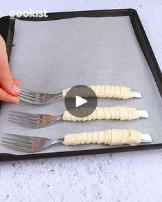 a person is holding three forks in front of a tray with four pieces of food on it