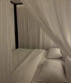 a bed with white sheets and pillows in a room that has curtains on the walls