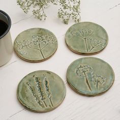 four ceramic coasters with flowers on them next to a coffee cup and flower pot