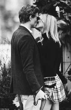 a man and woman kissing each other while standing next to each other in front of some bushes