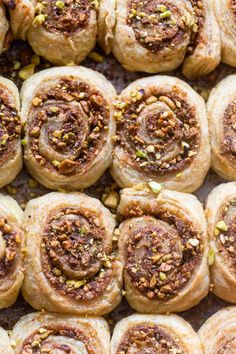 many different types of bread rolls on a baking sheet with pistachio toppings