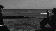 two people are sitting on the rocks near the ocean and one is holding a cell phone