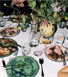 the table is set with plates, silverware and vases filled with flowers on it