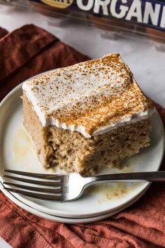 a piece of cake on a white plate with a fork next to it and a box of organic milk in the background