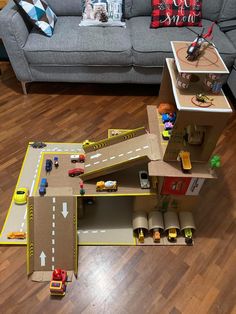 a toy train set with cars and trucks on the floor next to a gray couch