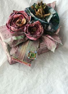 an open gift box sitting on top of a bed covered in paper and fabric flowers