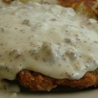 chicken fried with gravy on top of it and some potatoes in the background