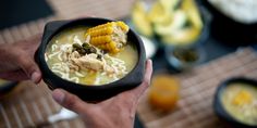 a person holding a bowl of soup with corn on the cob and other foods