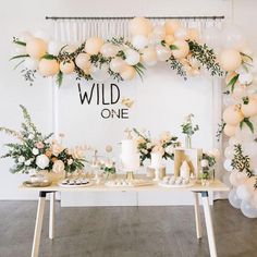 a table topped with lots of cake next to balloons and greenery on the wall