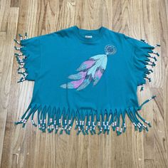 Vintage Feather Glitter Festival Boho Hippie Tasseled Graphic Print T Shirt USA XL Approx. Dimensions (lying flat) Chest (Pit to Pit): 23 in Top to Bottom(measured at start of tassels): 18 1/2 in Casual Blue Tops With Tassel Ties, Casual Festival Tops With Tassels, Casual Tops With Tassels For Festival, Cotton Tassel Tops For Festivals, Casual Short Sleeve Tops With Tassels, Bohemian Tops With Tassel Ties And Short Sleeves, Casual Short Sleeve Tops With Tassel Ties, Casual Crew Neck T-shirt With Fringe, Cotton Fringe Short Sleeve Tops