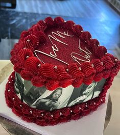 a heart shaped cake with red frosting and hearts on it's sides, sitting on a table