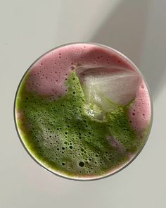 a drink in a glass filled with green and pink liquid on top of a white table