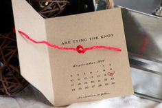 a paper bag with a red string tied around it and a calendar on the front that says are tying the knot