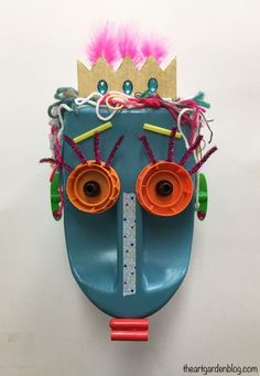 a blue mask with pink hair and two orange eyes, wearing a crown on top of it's head