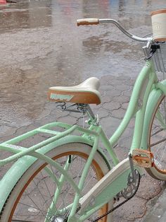 a green bicycle parked on the side of a road in the rain with an umbrella