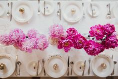 the table is set with plates, silverware and pink peonies on it