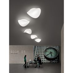 three people are sitting at a table in front of a clock and some lights hanging from the ceiling