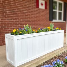 a white planter filled with yellow and blue flowers next to a brick wall in front of a house